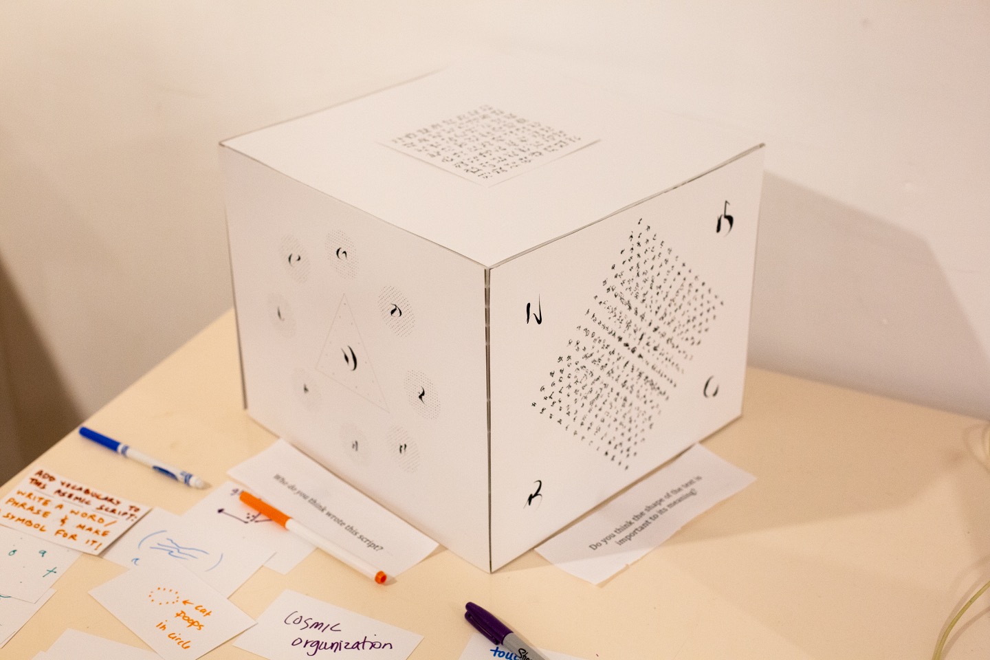 "A paper cube with asemic writing on four sides of the cube."