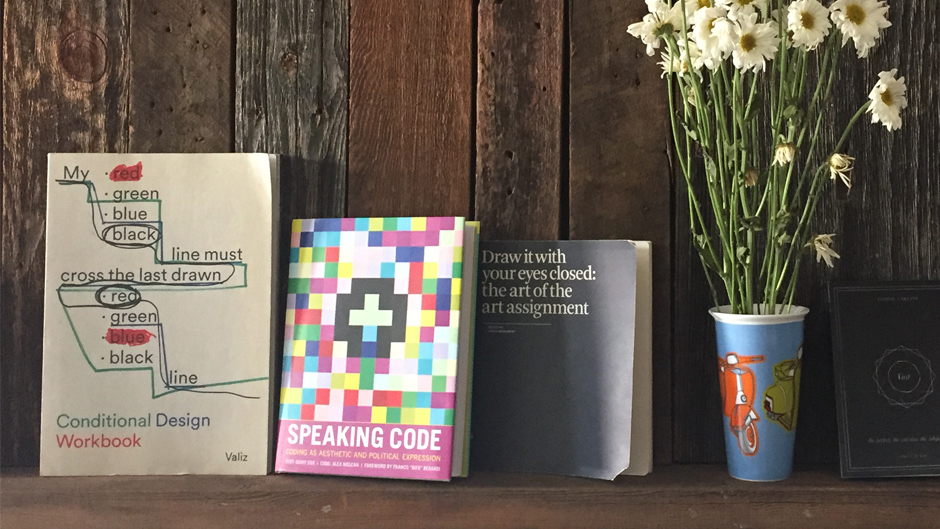 books next to flowers, the books are conditional design workbook, speaking code, and the art of the art assignment