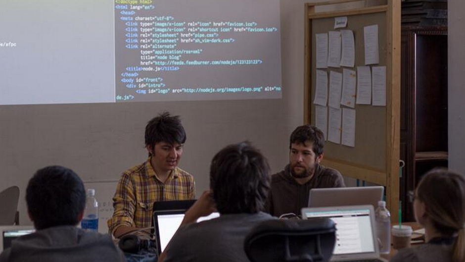sfpc students studying at laptops while example codes are projected behind