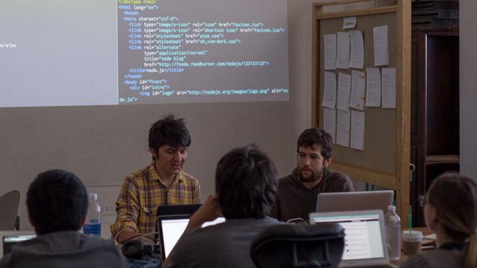 people working at laptops, in front of a projection of code