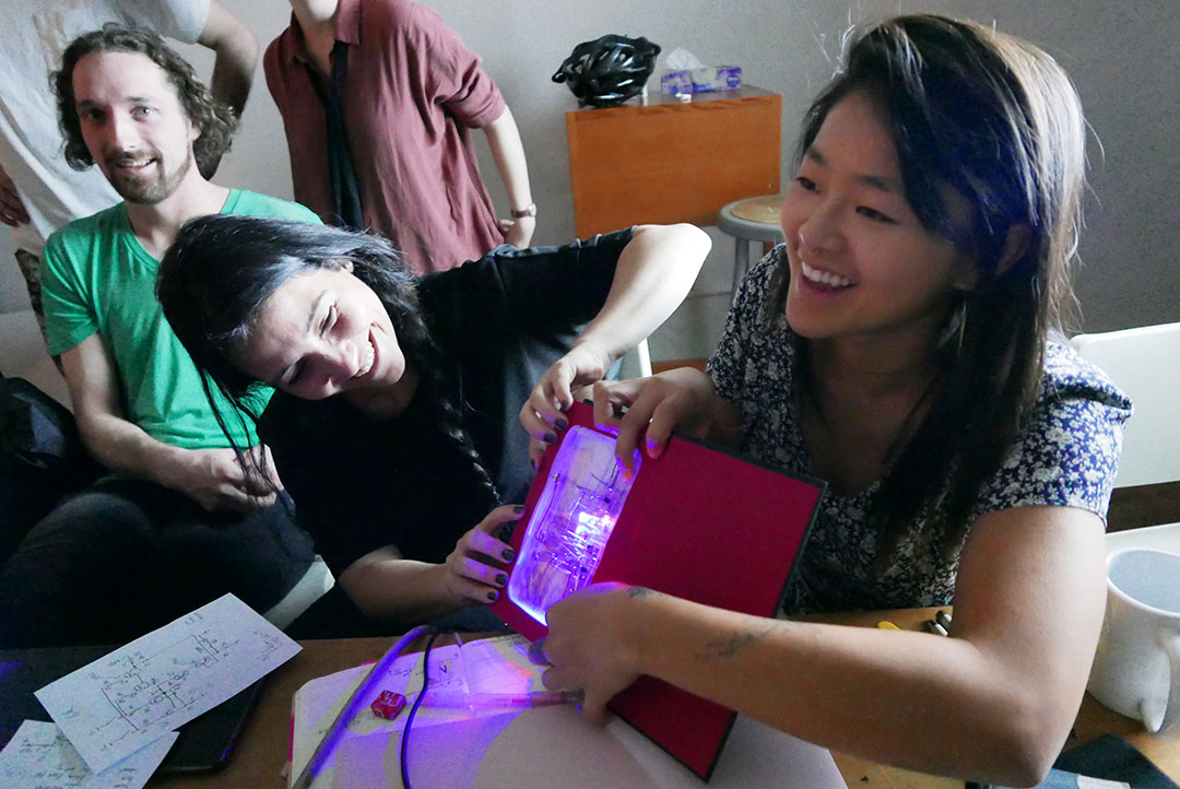 student projects, people around red box with electronics and lit interior