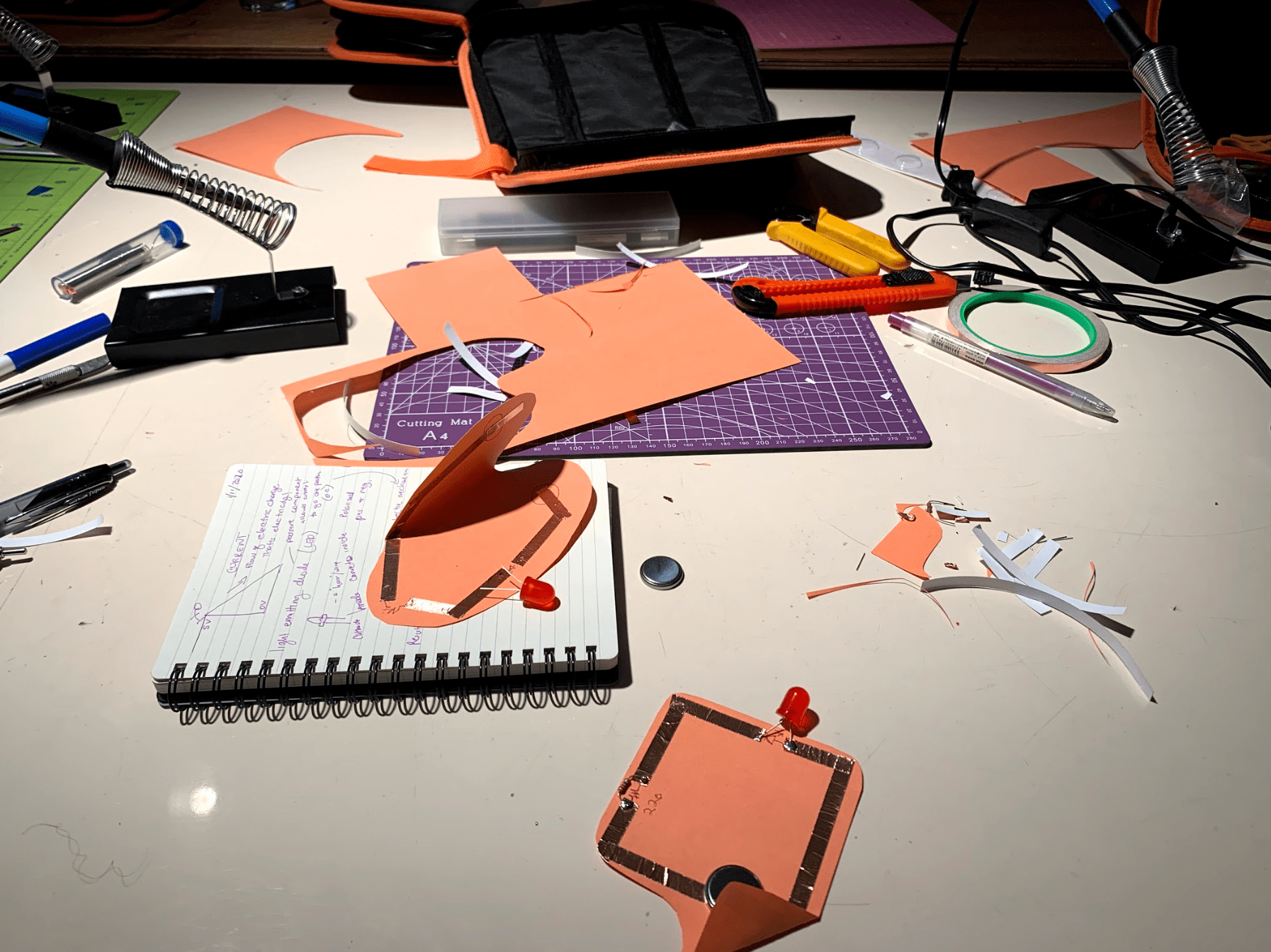 paper circuits, materials, notebooks, and sautering iron dispersed all over the table