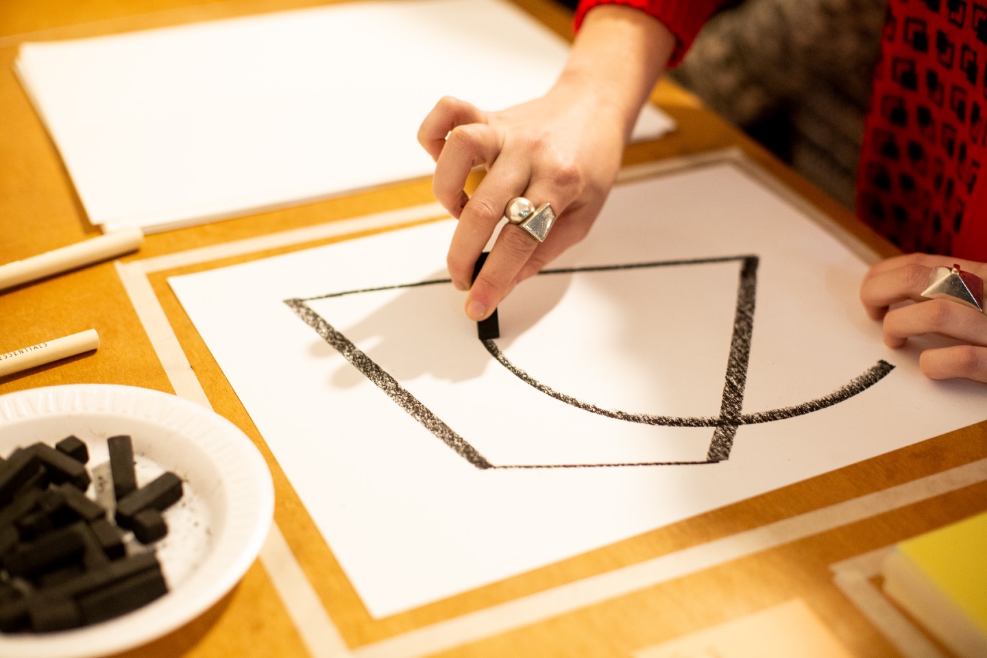 "A visitor following instructions from a card and drawing a shape in charcoal on paper."