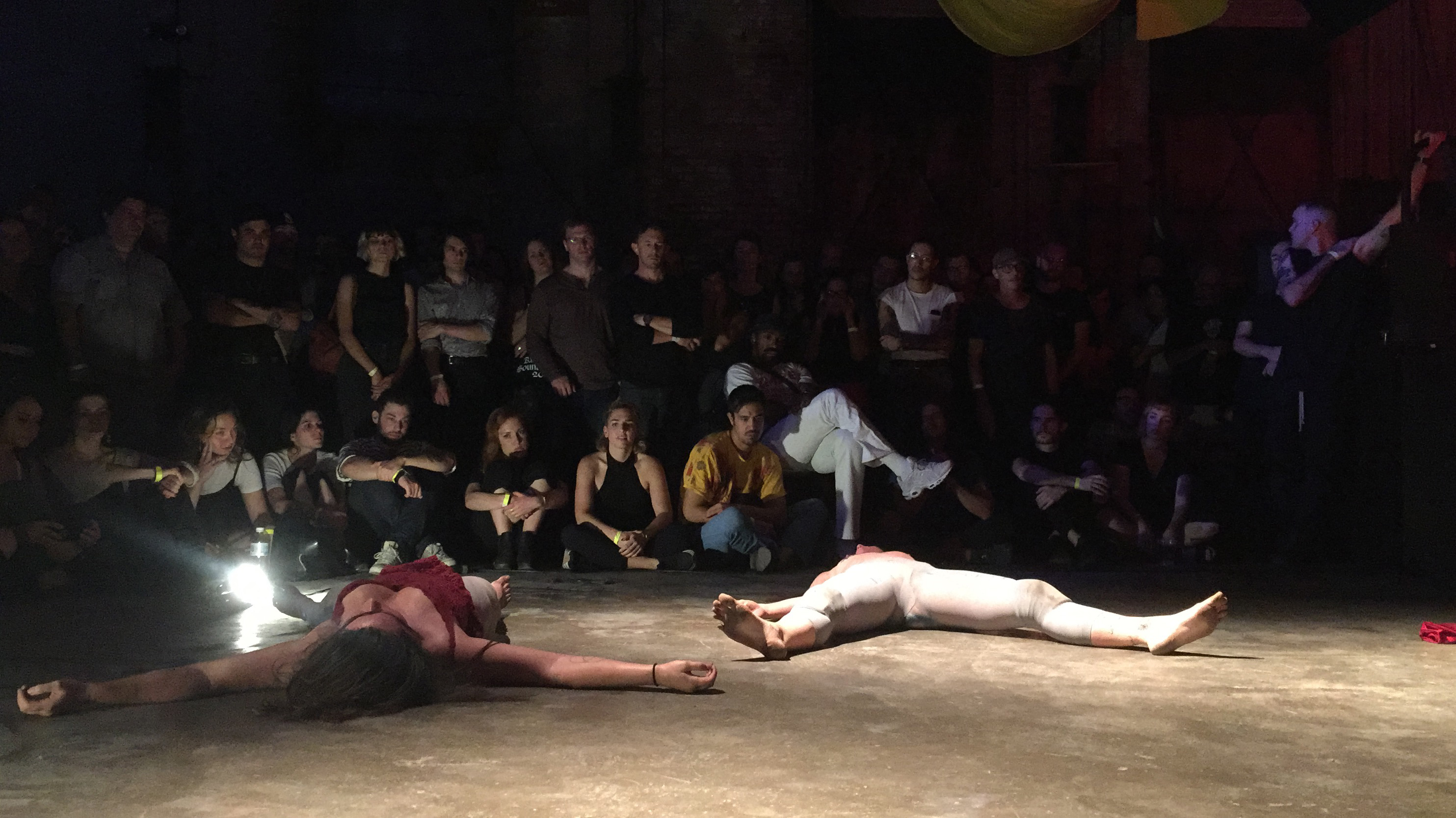 performers laying flat on a dance floor with darkly lit audience