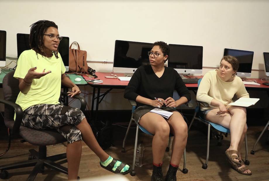 Three people discussing in front of computers