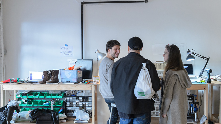 three people standing and talking in front of electronics workbench