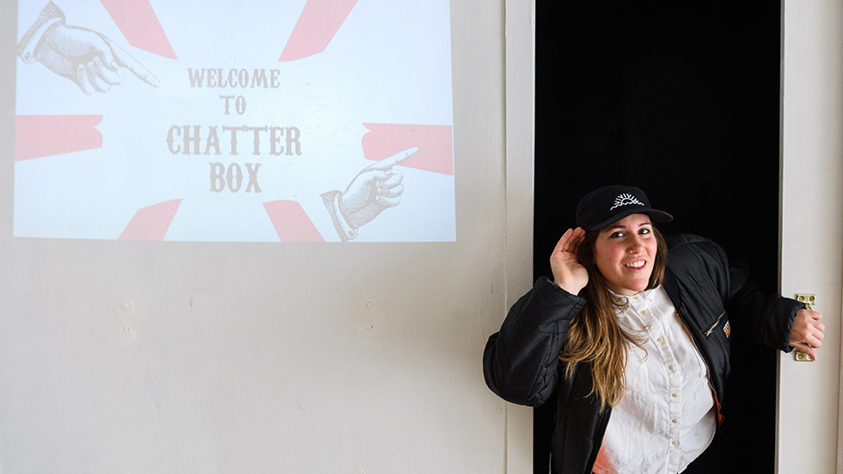 Katrina making hearing motion (hand cuped to ear) in front of welcome to the chatter box projection