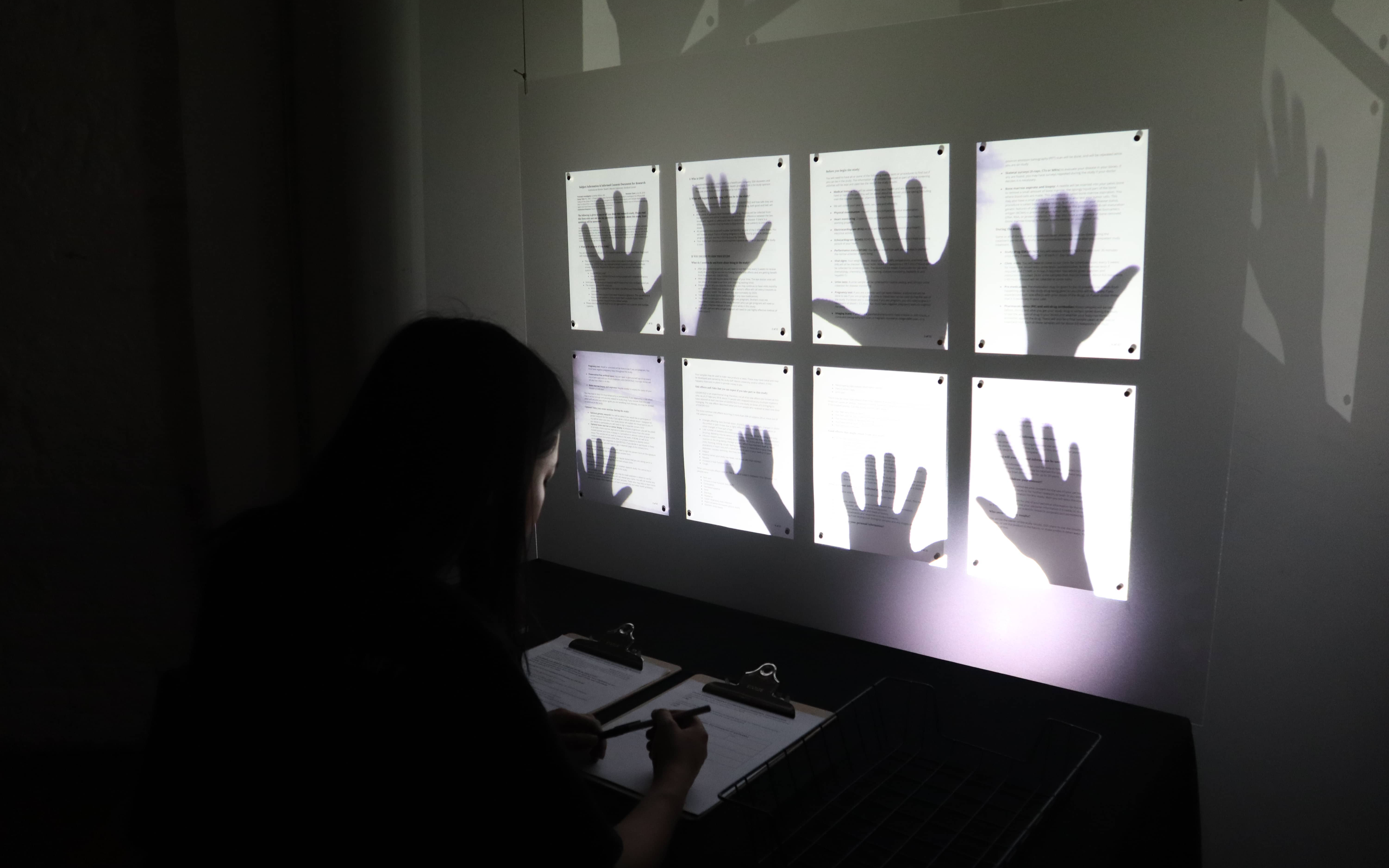 Shadows of hands shown behind pieces of paper on wall while person signs form