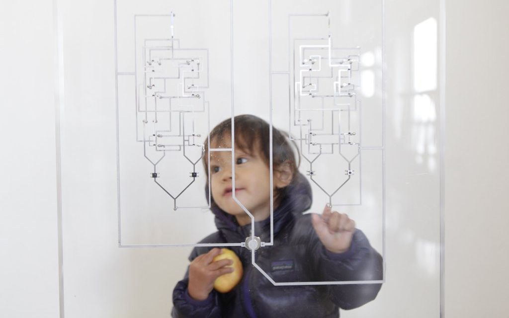 In the foreground a circuit board printed on glass, in the background a child